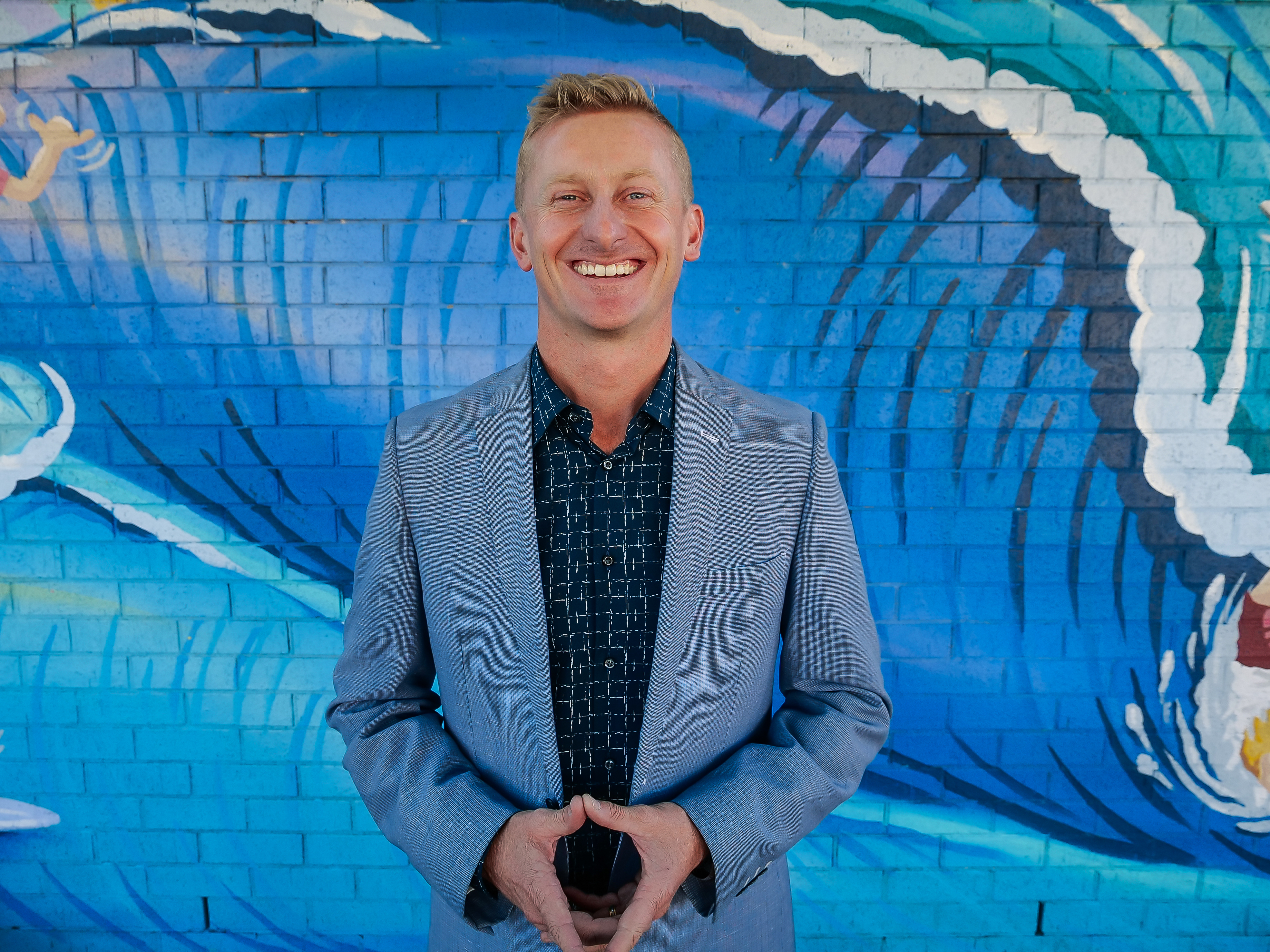 A man standing and smiling in front of a wall